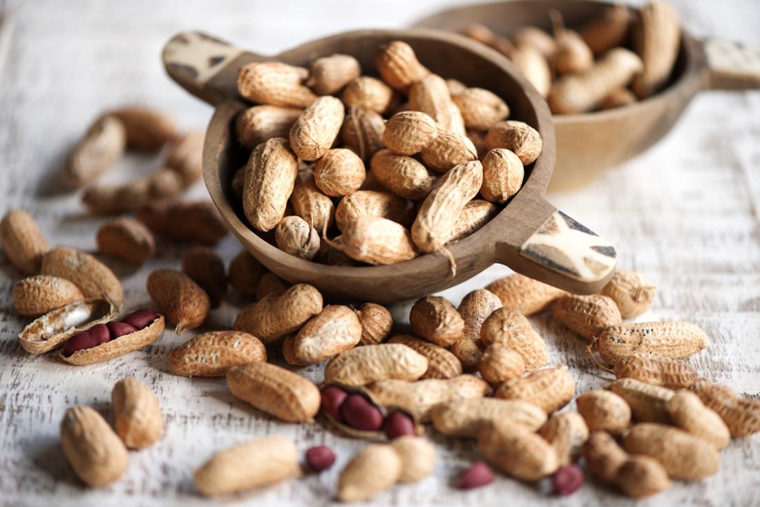 Peanuts in and out of shells spilling out of wooden bowl.